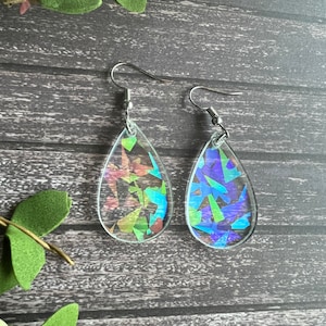 May include: A pair of iridescent teardrop-shaped earrings with a silver hook. The earrings are filled with small, colorful, iridescent pieces.