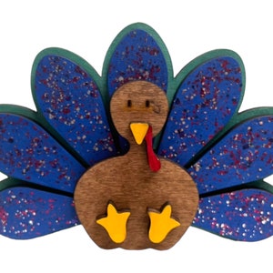 May include: A wooden turkey ornament with a blue and green patterned tail. The turkey has a brown body, red wattle, and yellow feet.