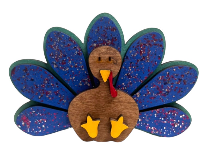May include: A wooden turkey ornament with a blue and green patterned tail. The turkey has a brown body, red wattle, and yellow feet.