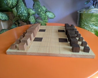 May include: A wooden chess set with light and dark wood squares. The chess pieces are cube-shaped, with light brown and dark brown pieces arranged on the board. The board is on an orange surface.