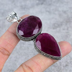 May include: A silver pendant with two large, faceted, purple gemstones. The pendant has a detailed, ornate design.