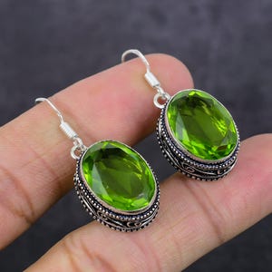 May include: A pair of silver earrings with green oval-shaped gemstones. The earrings have a detailed silver design around the gemstones.