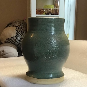 May include: A green ceramic vase with a floral design. The vase has a wide base and a narrow neck.