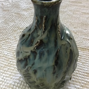 Könnte beinhalten: Eine handgefertigte Keramikvase mit strukturierter Oberfläche und einzigartiger, organischer Form. Die Vase weist eine Mischung aus Blau-, Türkis- und Brauntönen auf und schafft ein optisch ansprechendes, künstlerisches Stück. Die Vase ist etwa 20 cm hoch.