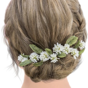 May include: A woman's hairstyle featuring a white flower crown. The crown is made of small white flowers and green leaves. The flowers are arranged in a circle around the woman's head.