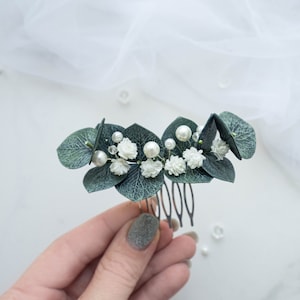 Op de afbeelding: Een groene eucalyptusbladeren haar kam met witte bloemen en parel accenten.