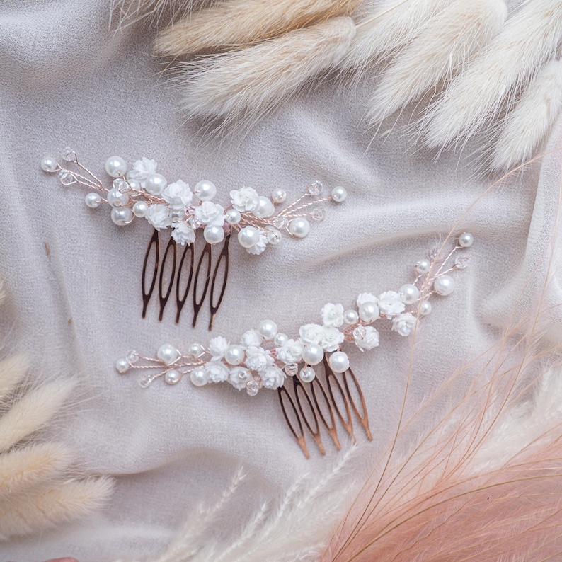 May include: Two hair combs featuring rose gold wire branches adorned with white floral accents, round white pearls, and small clear crystals. Each comb has five metal teeth and a curved design that extends outward with delicate wire detailing.