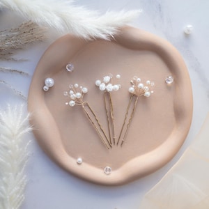 May include: Three gold-toned hair pins featuring delicate wire branches adorned with small white faux pearls and clear beads. Each pin has a wavy U-shaped base, creating a floral-inspired arrangement of beads and pearls on thin metallic stems.