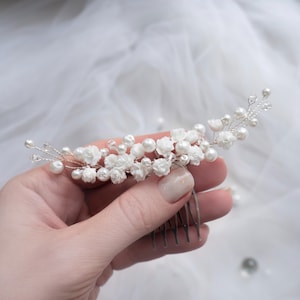 May include: A hair comb featuring a silver-toned wire base adorned with small white floral accents, round white faux pearls, and clear crystal beads. The decorative arrangement is spread across the top of the comb, creating a curved, branch-like design.