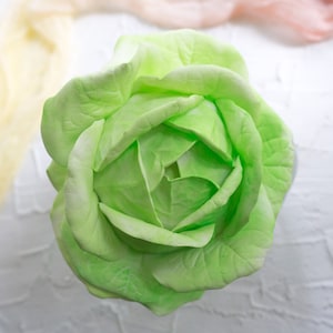 May include: A single, light green artificial rose with a closed bud. The rose is made of fabric and has a realistic appearance.