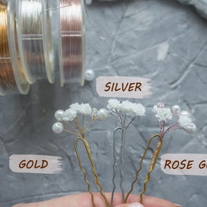 May include: Three hair pins featuring small white flowers and white beads on gold, silver, and rose gold wire stems. The pins are labeled with the text GOLD, SILVER, and ROSE GOLD. Three spools of matching gold, silver, and rose gold wire are visible.