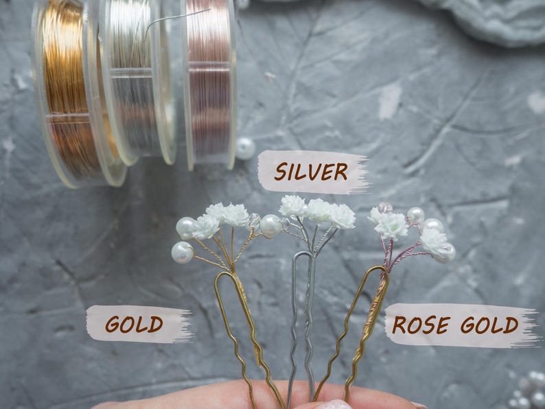 May include: Three hair pins featuring small white flowers and white beads on gold, silver, and rose gold wire stems. The pins are labeled with the text GOLD, SILVER, and ROSE GOLD. Three spools of matching gold, silver, and rose gold wire are visible.