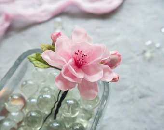 May include: A pink fabric flower with a dark brown stem and leaves. The flower is in a clear glass vase filled with clear glass beads.