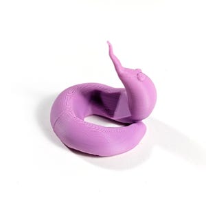 May include: A 3D printed purple worm figurine. The worm is curled up in a circle with its tail pointing up.