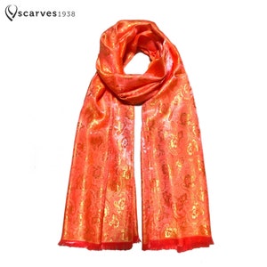 Puede incluir: Una bufanda de seda naranja brillante con un patrón floral dorado y flecos rojos.