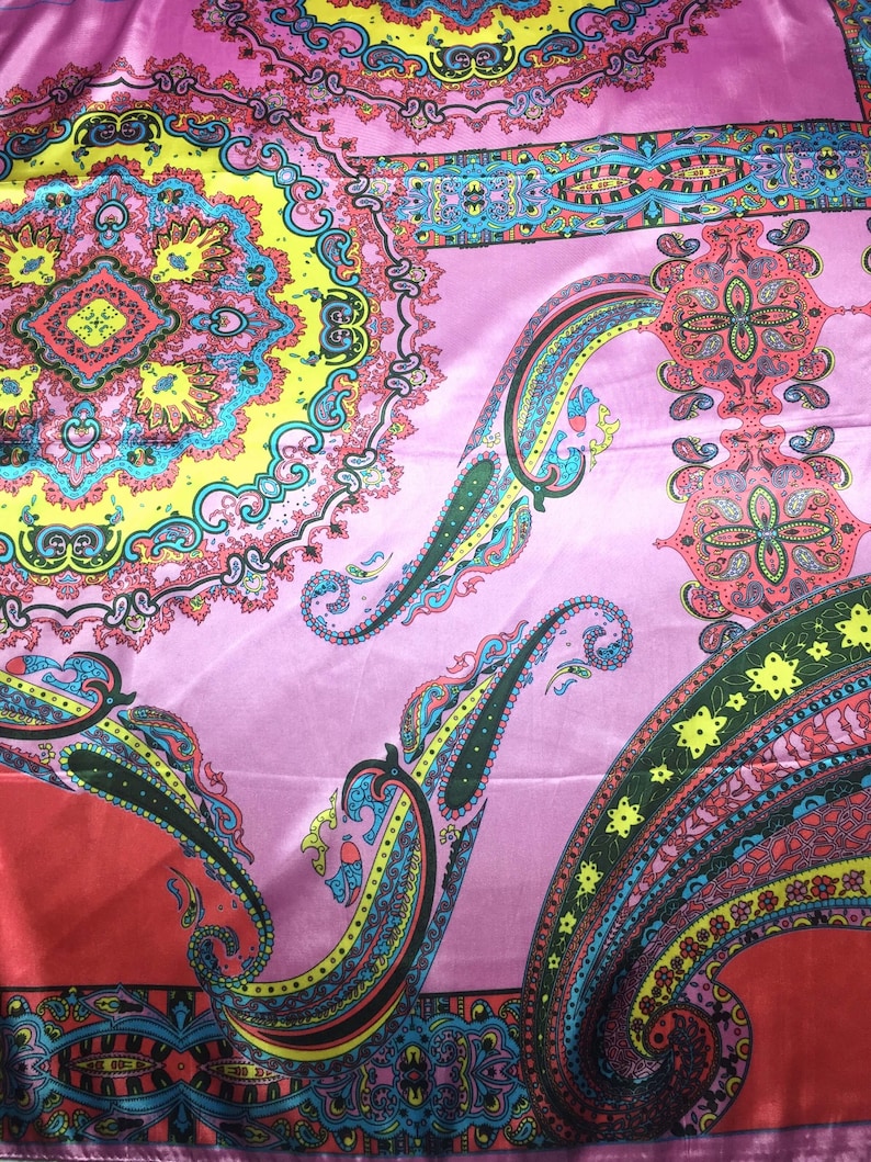 May include: A satin fabric scarf featuring a vibrant, multi-colored paisley and mandala pattern. The design includes shades of pink, yellow, red, turquoise, and black, with intricate floral and teardrop motifs arranged in a repeating, symmetrical layout.