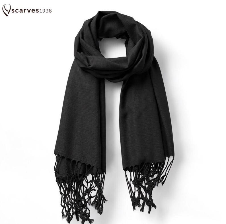 May include: A black scarf with fringe detailing. The scarf is draped and displayed against a white background. The brand name "scarves1938" is in the upper left corner.