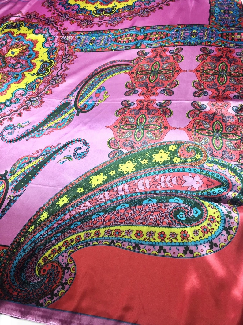 May include: A vibrant silk scarf featuring a complex paisley pattern in shades of hot pink, bright yellow, turquoise, and red. The design includes intricate floral motifs, swirling teardrop shapes, and geometric borders printed on a smooth fabric.