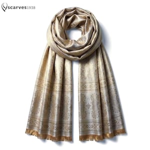 May include: A metallic gold scarf featuring an intricate woven floral pattern and a repeating geometric border design. The scarf has a soft sheen and is finished with delicate fringe at both ends. The text "scarves1938" appears in the corner.