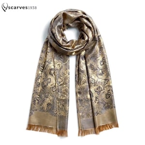 Puede incluir: Una bufanda rectangular con un patrón de cachemira en dorado metálico y gris oscuro. La bufanda tiene un acabado brillante con un borde dorado sólido en los extremos inferiores y detalles de flecos delicados. El texto "scarves1938" aparece arriba a la izquierda.
