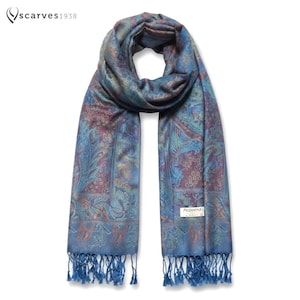 Puede incluir: Una bufanda pashmina azul con un intrincado patrón de cachemira en tonos morado, verde azulado y dorado. La bufanda incluye una etiqueta tejida que dice PASHMINA y tiene flecos largos anudados en ambos extremos. El texto scarves1938 es visible.