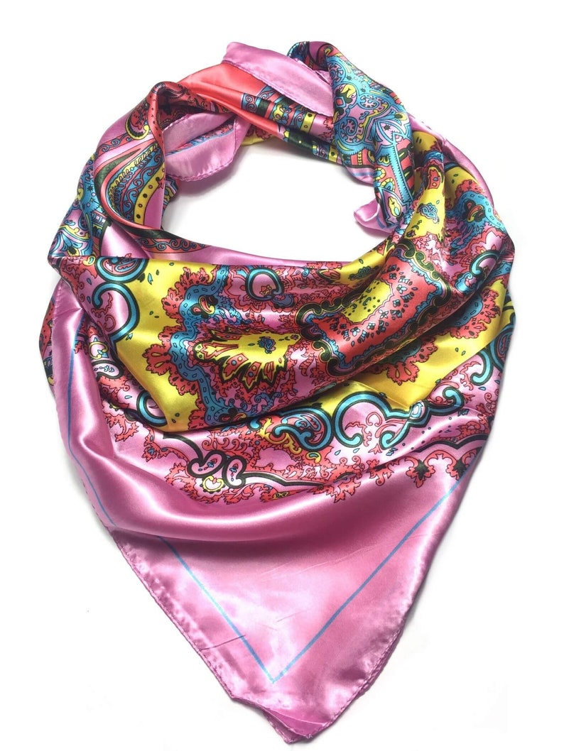 May include: A square satin scarf featuring a vibrant paisley pattern in shades of pink, yellow, and turquoise. The scarf is folded into a triangular shape, displaying a smooth, reflective surface with intricate decorative motifs and a thin blue border.