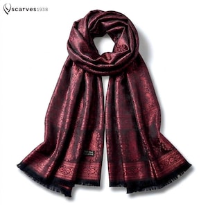 May include: A deep burgundy and black scarf featuring an intricate woven paisley pattern throughout the fabric. The scarf has a rectangular shape with fringed edges at both ends and a small black label with white text reading scarves1938.