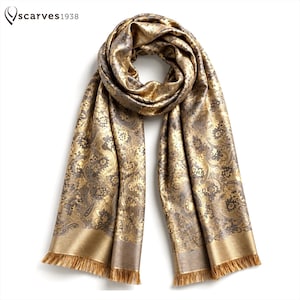 May include: A metallic gold and dark gray scarf featuring an intricate floral and paisley pattern throughout. The scarf has a looped top section and two long, hanging ends finished with a straight, fringed hem. The text "scarves1938" is visible.