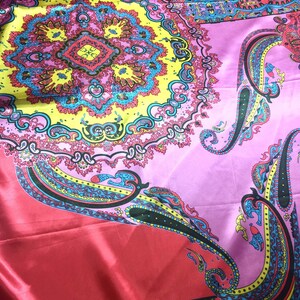 May include: A vibrant fabric featuring a large, intricate circular mandala pattern in yellow, pink, and blue. The design includes detailed paisley motifs and geometric shapes, set against a smooth, shiny, satin-like material with a bright pink base.