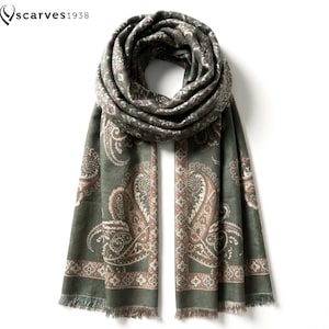 Puede incluir: Una bufanda rectangular en un tono verde oliva apagado con un patrón de cachemira detallado en tonos beige, marrón y crema. La bufanda incluye un borde decorativo con motivos florales y bordes con flecos. El texto "scarves1938" es visible.
