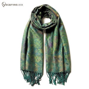May include: A long rectangular scarf featuring a complex paisley pattern in shades of emerald green, teal, and hints of purple and gold. The scarf has a woven texture and is finished with long, matching green fringe along both bottom edges.