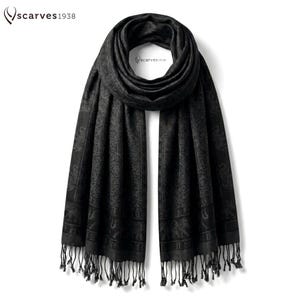 Puede incluir: Una bufanda negra con un patrón de elefantes en tonos a juego, un borde decorativo y flecos en los extremos. El texto "scarves1938" aparece en la esquina superior izquierda y en una pequeña etiqueta en el centro de la tela drapeada.