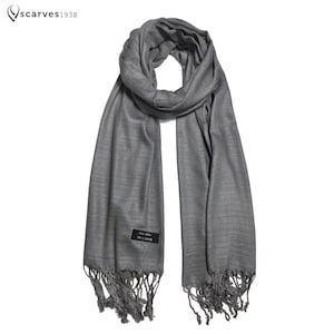 May include: A gray pashmina scarf with fringe on the ends. The scarf is folded in half and draped over a white background.