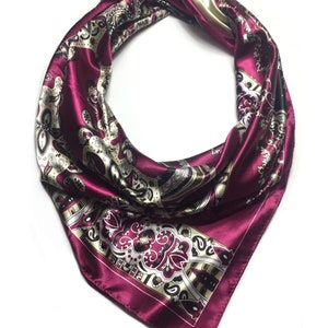 May include: A burgundy silk scarf with a paisley pattern in gold, black, and white. The scarf is tied in a knot at the top.