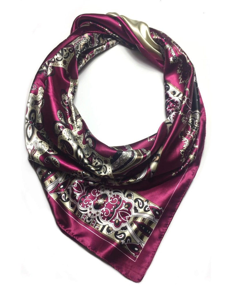 May include: A burgundy silk scarf with a paisley pattern in gold, black, and white. The scarf is tied in a knot at the top.