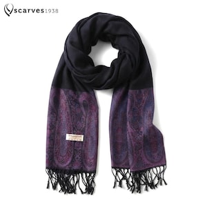 May include: A black scarf featuring a purple and blue paisley pattern on the ends and black fringe. The scarf includes a white rectangular tag with the text PASMINA and care symbols. The top left corner displays the text scarves1938 with a logo.