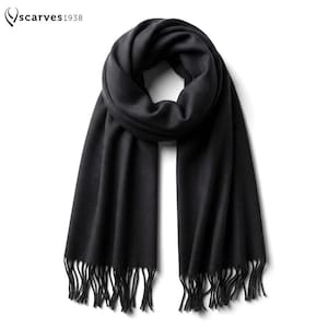 Puede incluir: Una bufanda negra lisa con textura suave y extremos con flecos. La bufanda est&aacute; anudada en la parte superior y cuelga en dos paneles largos y rectos. El texto "scarves1938" est&aacute; impreso en la esquina superior izquierda en una fuente negra.
