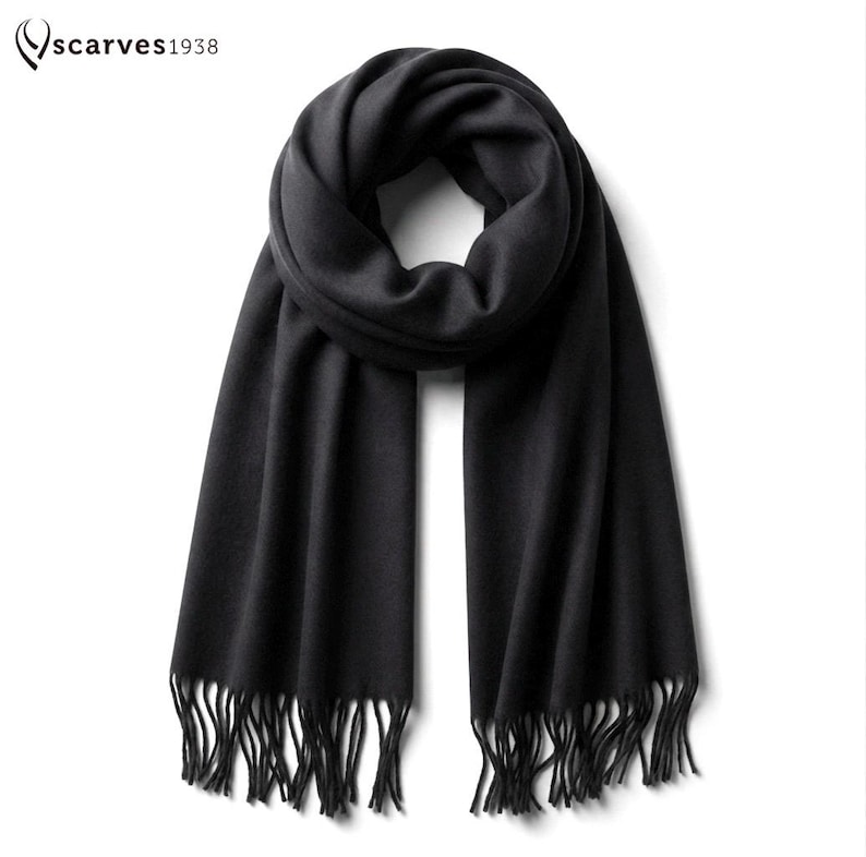 Puede incluir: Una bufanda negra lisa con textura suave y extremos con flecos. La bufanda est&aacute; anudada en la parte superior y cuelga en dos paneles largos y rectos. El texto "scarves1938" est&aacute; impreso en la esquina superior izquierda en una fuente negra.