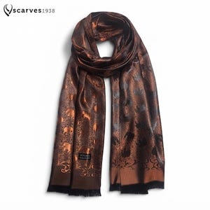 May include: A rectangular scarf in a deep bronze and black colour palette featuring a repeating elephant pattern. The scarf has a subtle sheen, a woven texture, and a fringed hem at both ends. A small black label is visible near the bottom edge.