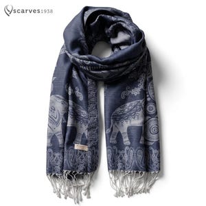 Op de afbeelding: Een donkerblauwe sjaal met een herhalend lichtgrijs olifantenpatroon, decoratieve paisley-randen en lange franjes aan de uiteinden. De sjaal bevat een klein rechthoekig label met de tekst "PASMINA" en het logo "scarves1938" in de hoek.