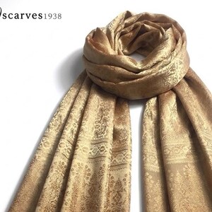 May include: A gold-colored scarf featuring an intricate, repeating jacquard pattern with floral and geometric motifs. The scarf is draped in a circular loop at the top with two long ends hanging down. The text "scarves1938" appears in the top left corner.