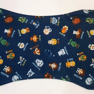 May include: A navy blue baby bib featuring a repeating pattern of Star Wars characters and names. The bib has a unique hourglass shape and is made of soft fabric. Characters include Yoda, C-3PO, and Princess Leia.