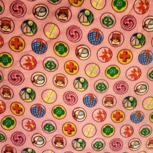 May include: Pink fabric with a repeating pattern of circular designs. Each circle contains various colorful illustrations, including a cross, a swirl, a globe, a leaf, and an owl. The text "GS WAY" is also present.