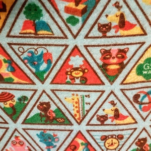 May include: A light blue fabric with a repeating pattern of colorful triangular shapes. Each triangle contains a different cartoon animal or object, such as a cat, dog, raccoon, and monkey. The words "GS WAY" are visible in one triangle.