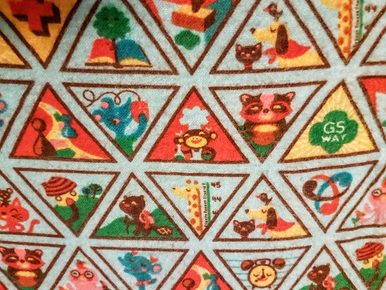 May include: A light blue fabric with a repeating pattern of colorful triangular shapes. Each triangle contains a different cartoon animal or object, such as a cat, dog, raccoon, and monkey. The words "GS WAY" are visible in one triangle.