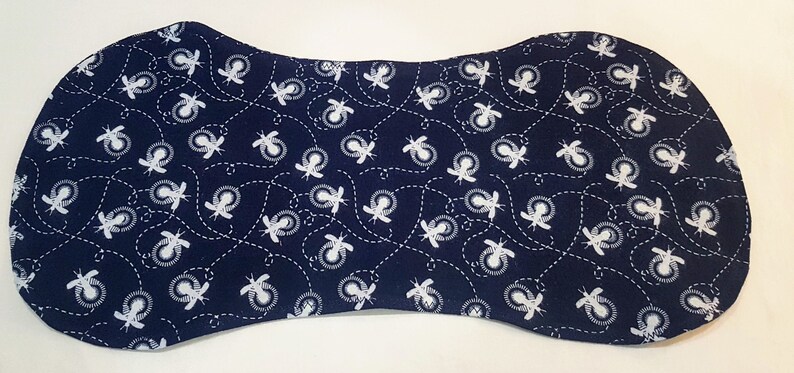 May include: Navy blue baby bib with a white bee pattern. The bib is a unique shape, with a curved top and bottom, and a narrower center. The bee design is repeated across the surface.