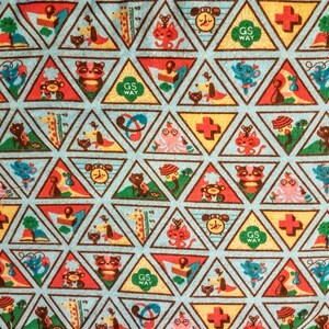 May include: A light blue fabric with a repeating pattern of colorful triangular patches. Each triangle features a different illustration of animals, objects, and the text "GS WAY". The patches are outlined in brown.