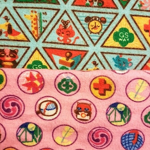 May include: Two fabrics with colorful patterns. The top fabric is light blue with brown-lined triangles containing cartoon animals and the text "GS WAY". The bottom fabric is pink with circular designs featuring various graphics and the text "GS WAY".