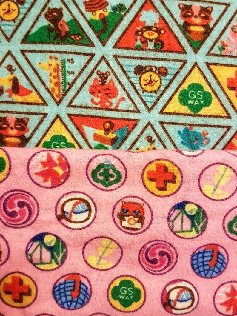 May include: Two fabrics with colorful patterns. The top fabric is light blue with brown-lined triangles containing cartoon animals and the text "GS WAY". The bottom fabric is pink with circular designs featuring various graphics and the text "GS WAY".
