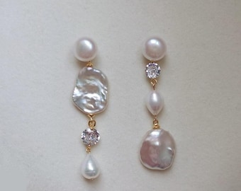 Puede incluir: Un par de pendientes desparejados con perlas blancas y piedras facetadas transparentes en metal dorado. El pendiente izquierdo tiene una perla redonda, una perla barroca irregular grande, una piedra transparente y una perla pequeña en forma de lágrima. El derecho tiene una perla redonda, una piedra transparente, una perla ovalada pequeña y una perla barroca irregular grande.